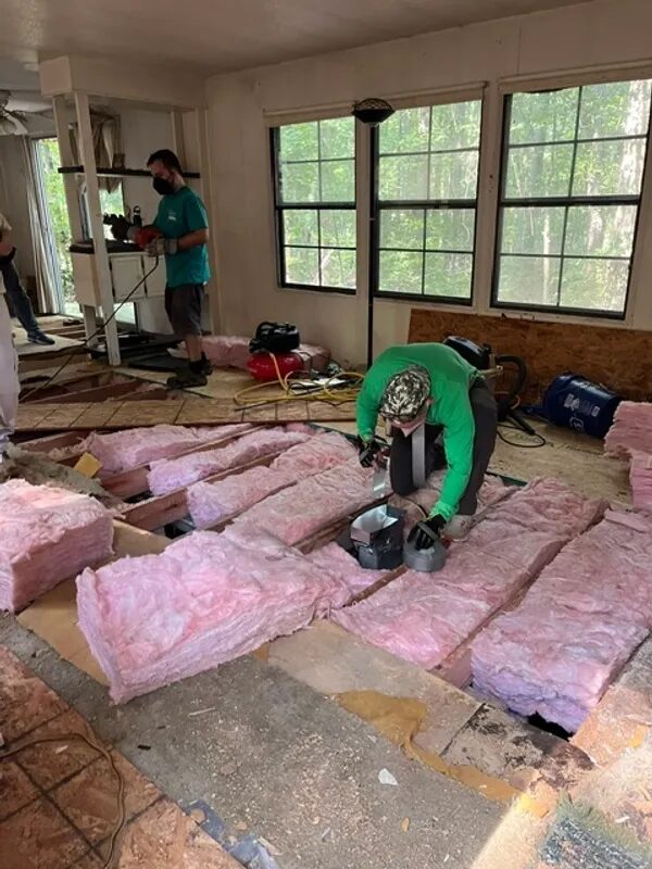 Volunteers replacing a rotted subfloor and laying new insulation inside a home